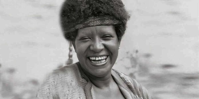Smiling woman wearing a patterned headband, outdoors; black-and-white photo.