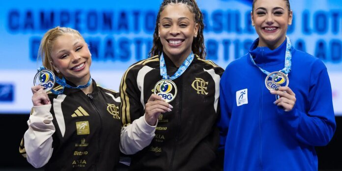 Three female athletes on a podium proudly displaying their medals, center winner in a black and gold jacket.