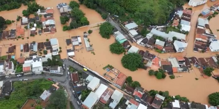 Aerial view of a flooded town with brown water surrounding houses and streets, trees partially submerged in water.