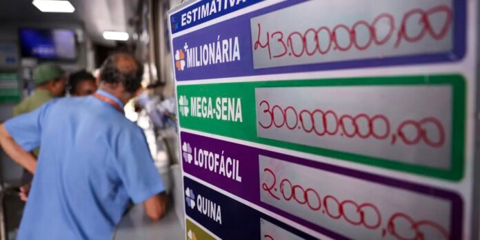 Close-up of a colorful lottery prize board with amounts for Mega-Sena and others; medical staff blurred in the background in blue scrubs.
