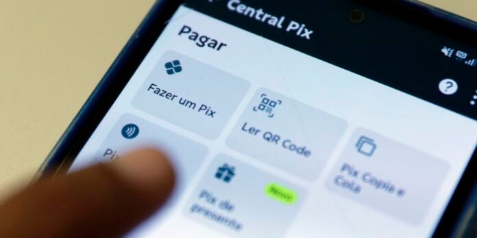 Tela do app Central Pix com opções de pagamento: Fazer um Pix, Ler QR Code, Copiar e Colar (Cópia) e outras funções; mão próxima ao toque.