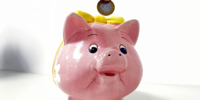 Pink ceramic piggy bank with a yellow bow, coin hovering above the slot as if about to be deposited