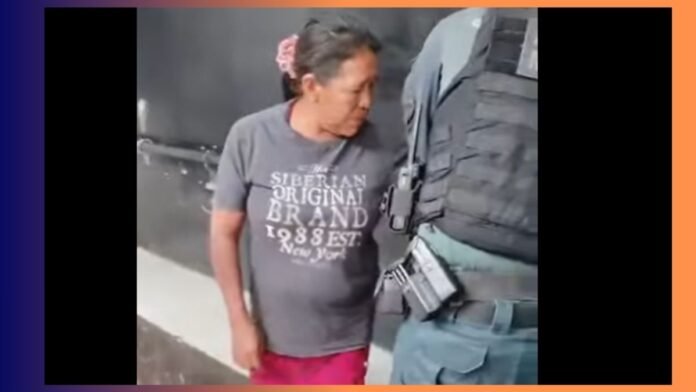 Woman in a gray t‑shirt stands beside a suited officer in tactical gear, looking toward the officer's belt.