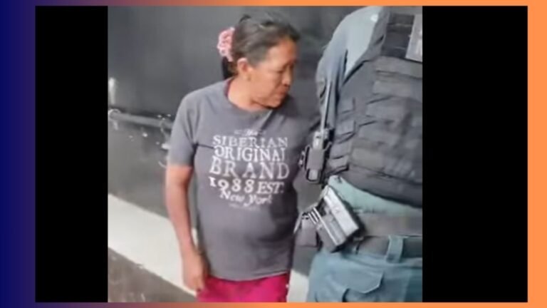 Woman in a gray t‑shirt stands beside a suited officer in tactical gear, looking toward the officer's belt.