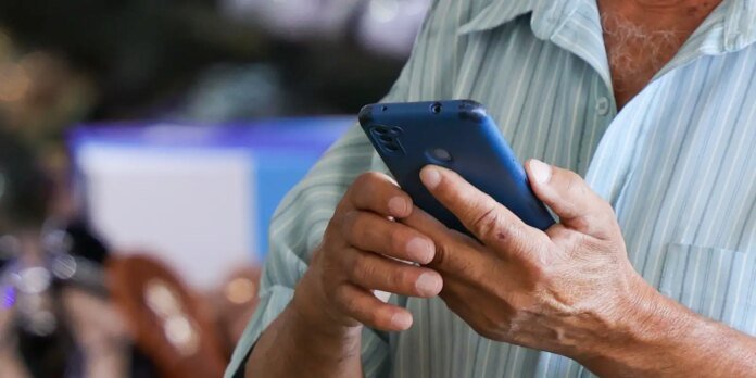Person wearing a light striped shirt holding a blue smartphone and touching the screen outdoors.
