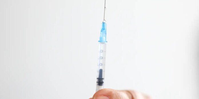 Close-up of a syringe with a blue needle cap held by a hand against a white background before an injection.