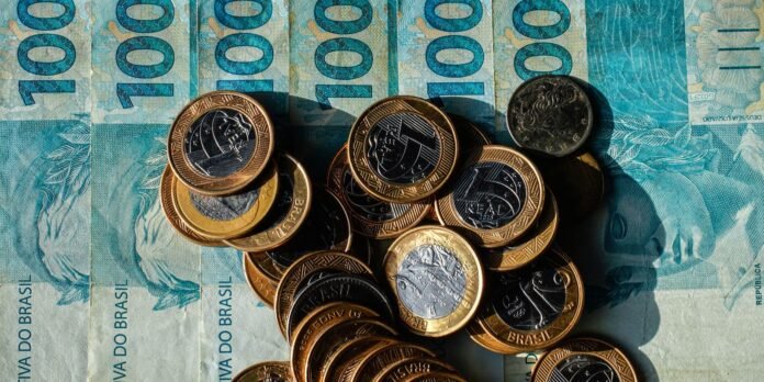 Pile of Brazilian real coins resting on blue 100 reais banknotes, symbolizing money and currency in Brazil.