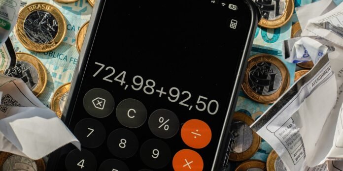 Phone screen shows a calculator app displaying the sum 724,98 + 92,50, surrounded by coins, banknotes, and receipts as a money-related scene