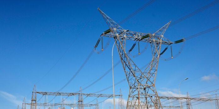 Lattice steel electricity transmission tower with multiple power lines against a clear blue sky.