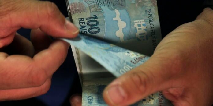Two hands hold and fold a blue 100 euro banknote, showing the currency being counted or handled.