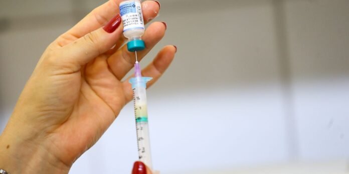 Close-up of a hand with red nail polish drawing liquid from a small vial into a syringe.