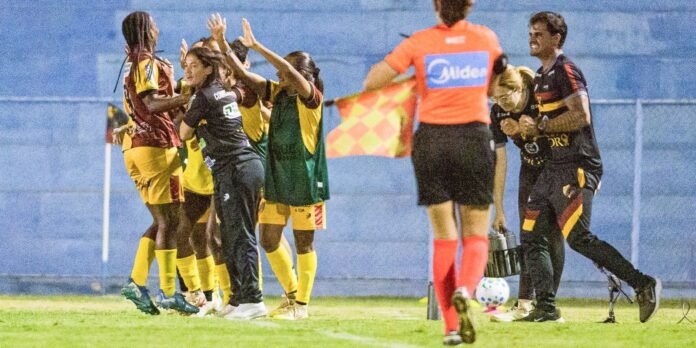 Group of female soccer players celebrate a goal, high-fiving near the sideline as a referee in orange looks on.