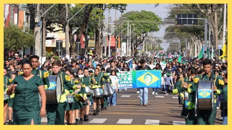 Large crowd in a city street parade; marching band in green uniforms plays drums, with a Brazilian flag in the foreground.