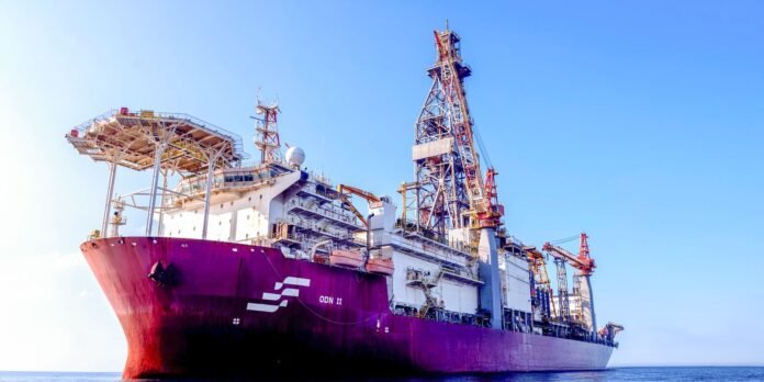 Offshore support vessel with a purple hull and complex crane structures against a clear blue sky.
