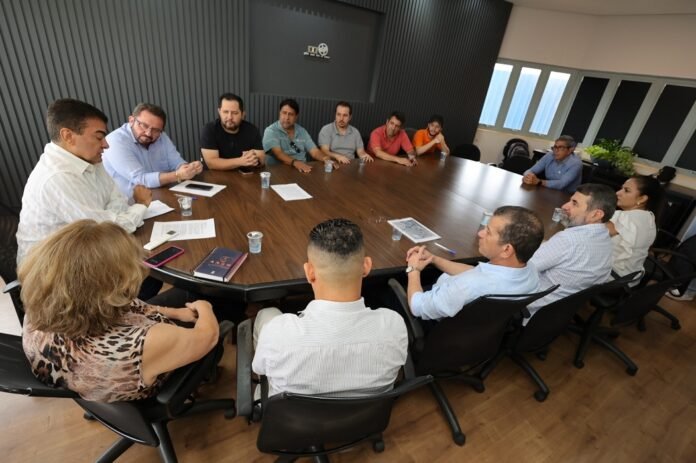 People sit around a large conference table in a boardroom, engaged in a meeting with papers and cups on the table.