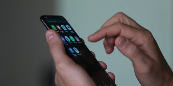 Close-up of hands holding a smartphone with colorful app icons on the screen, finger poised to tap a button.
