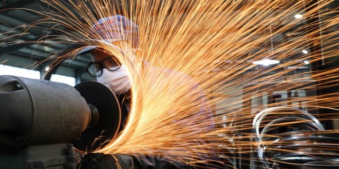 Worker wearing a mask and safety glasses operating a bench grinder, sparks flying in a workshop.