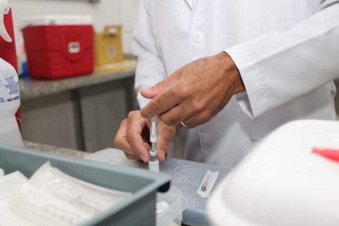 Lab technician in a white coat drawing liquid from a syringe into a vial on a lab counter