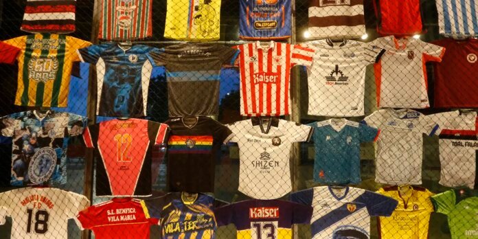 Colorful soccer jerseys hung on a mesh fence in a wall-style display.